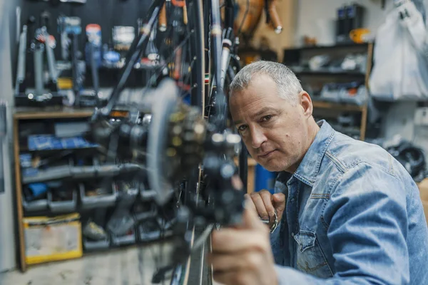 Service for bike with adept repairing bike. Bicycle mechanic in a workshop in the repair process. Stylish bicycle mechanic doing his professional work in workshop.