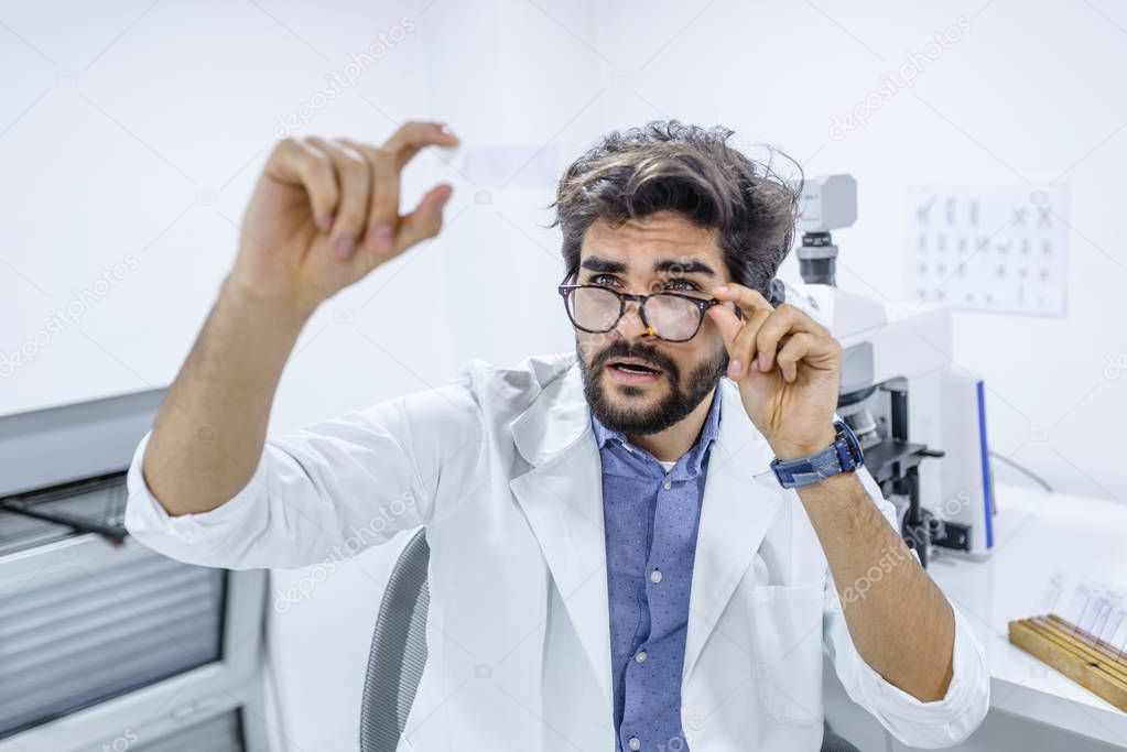 Male scientist examining microscope slide in medical lab. Researcher in front of microscope looking on microscope slide. Young researcher holding a microscope glass slide in the laboratory.