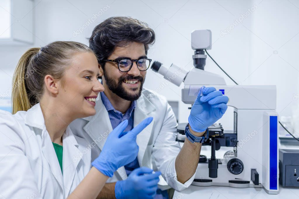 Two biotechnologists communicating while working on research in a laboratory. Colleagues working on their scientific research in laboratory. science, chemistry, technology, biology and people concept