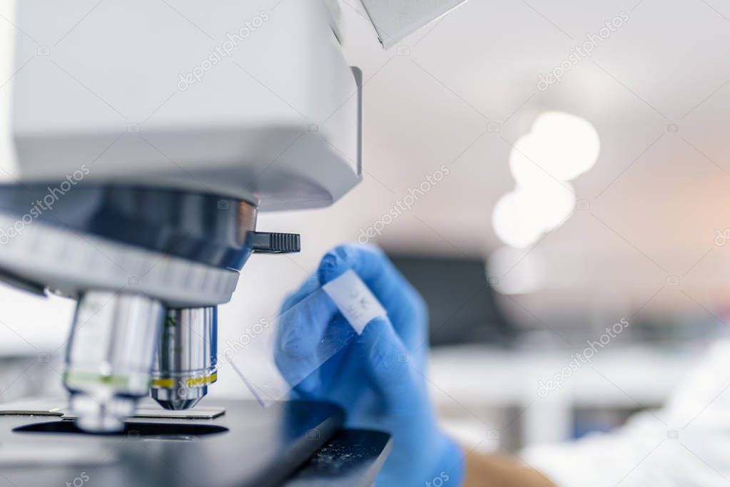 Close-up shot of microscope with metal lens at laboratory. Scientist hands with microscope close-up shot in the laboratory. Man in a laboratory microscope with microscope slide in hand