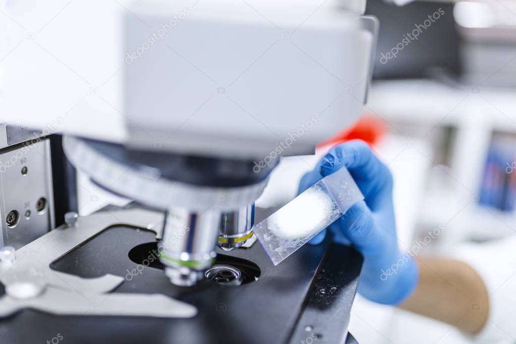 Man in a laboratory microscope with microscope slide in hand.  Young scientist doing some research. Male researcher using her microscope in a laboratory