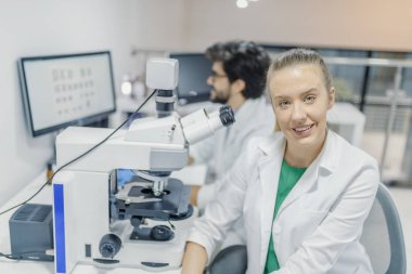 Laboratuvarda çalışan Beyaz üniformalı genç bilim adamları. Kameraya Laboratuvarı onun meslektaşım arka plan üzerinde seyir çekici gülümseyen fe erkek bilim adamı.