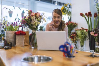Kadın çiçekçi çiçek dükkanında kasaya dizüstü bilgisayar kullanarak. Laptop onun dükkanında çalışan küçük çiçek dükkanı sahibi.