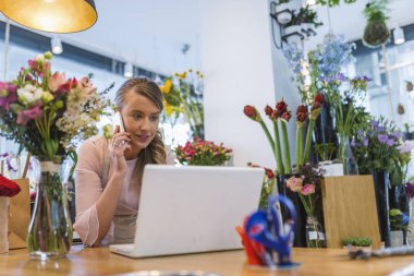 Mutlu çiçekçi çiçek dükkanında teknolojilerini kullanarak. Çiçekçi internetten sipariş alma. Çiçekçi online çiçek Shop arabirimini kullanarak. Ona çiçek dükkanında dizüstü bilgisayar kullanırken cep telefonda konuşurken çiçekçi