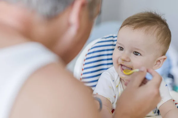 父摂食赤ちゃん男の子の高椅子 陽気な父は スプーンからお粥を食べる彼の幼い息子を教えています キッチンの小さな息子を餌の父 スプーンから父フィード赤ちゃん — ストック写真