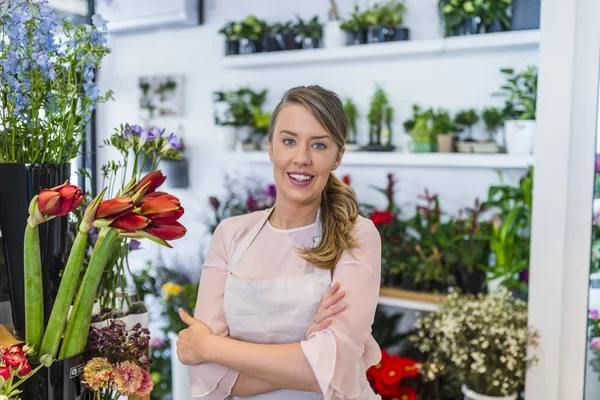 Beautiful young florist in flower shop. Portrait of owner of flower shop. Portrait of beautiful caucasian girl self-employed in flower shop, smiling and looking at camera. Horizontal shape, waist up