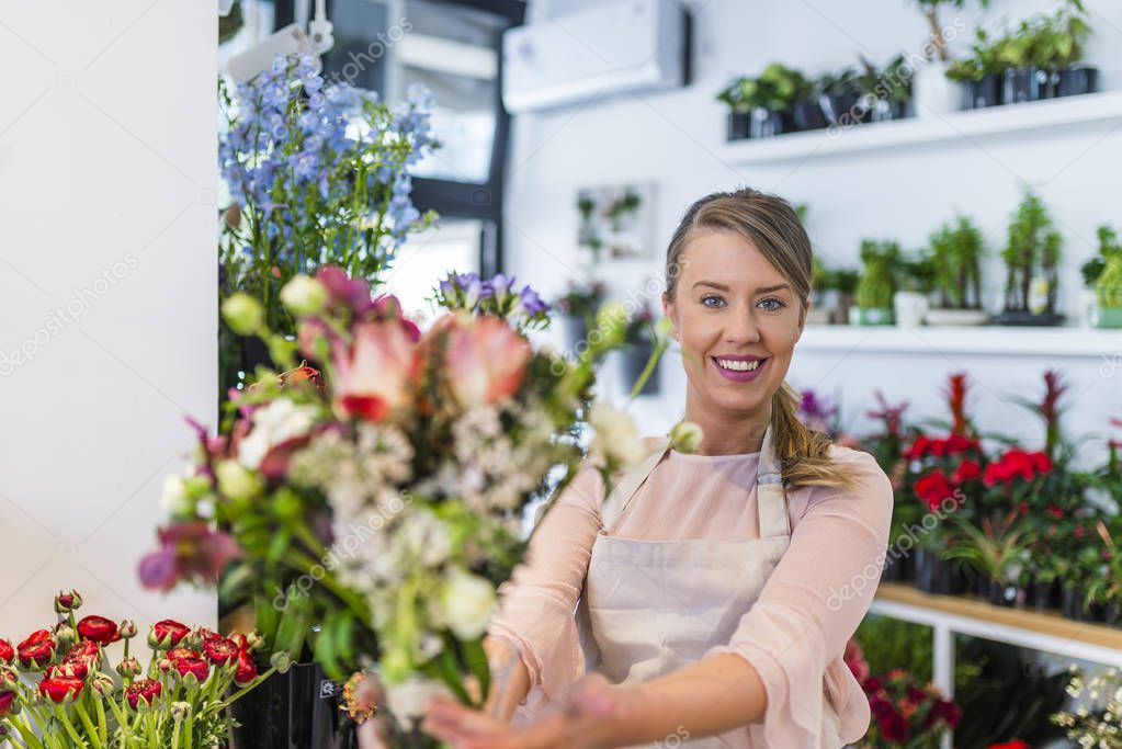 Portrait of a florist offering flowers at the counter in the florist shop. Young woman giving bouquet of flowers. Portrait of a happy florist offering and sale flowers at the counter in the florist shop. Florist giving beautiful flower bouquet to cli