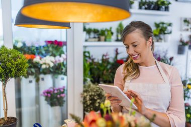Genç sahibi tarafından tablet emir online çiçekçi dükkanı. Küçük işletme. Güzel kadın çiçekçi çiçek dükkanında tablet ile. Çiçekçi online çiçek Shop arabirimini kullanarak