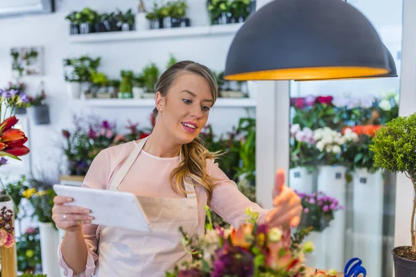 タブレットでオンラインで注文を取って花屋女性 タブレットの花屋で働く女性の花屋 タブレットを使用して アプリで配送の手配 花の店の販売員の作物ショット — ストック写真