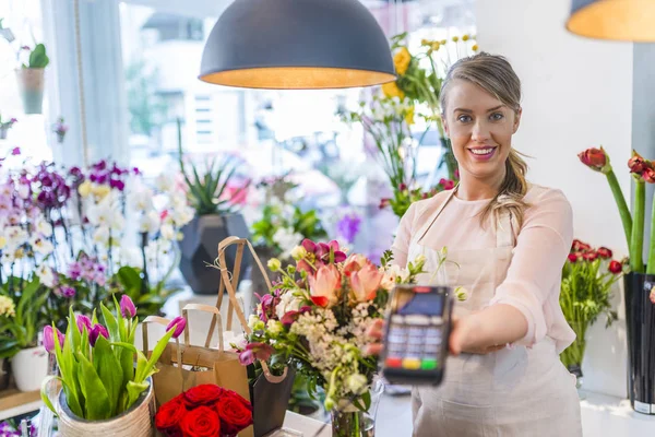 POS-terminal in the shop. Woman is offering payment terminal for paying with credit card. Mobile payment PayPass in flowers shop.