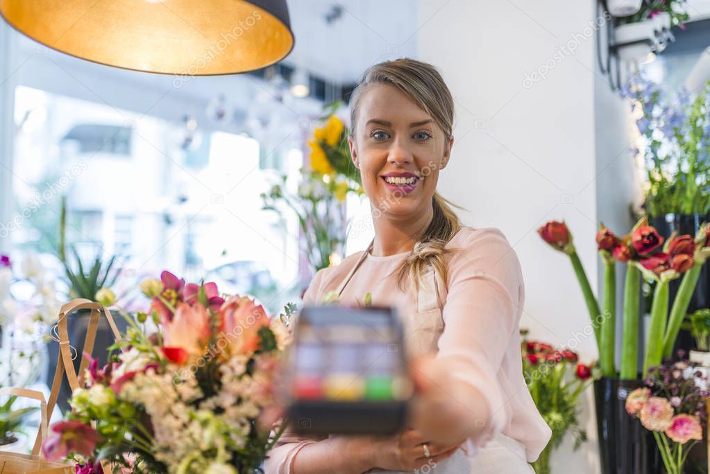 Customer paying with credit card in florist shop. Woman is offering payment terminal for paying with credit card. Florist shop owner holding credit card terminal. Credit card payment