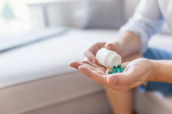 Man holding pills on hand. Pills in hands. Medicine and health care concept. Hand spilling pills for the pain of a bottle in the living room. Healthy lifestyle, medicine, nutritional supplements and people concept