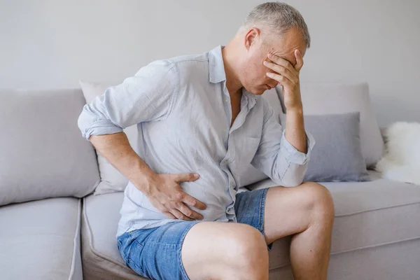 Hand of old man holding stomach suffering from pain, diarrhea, indigestive problem. A middle-aged man has a stomach ache. Unhappy man suffering from stomach ache at home