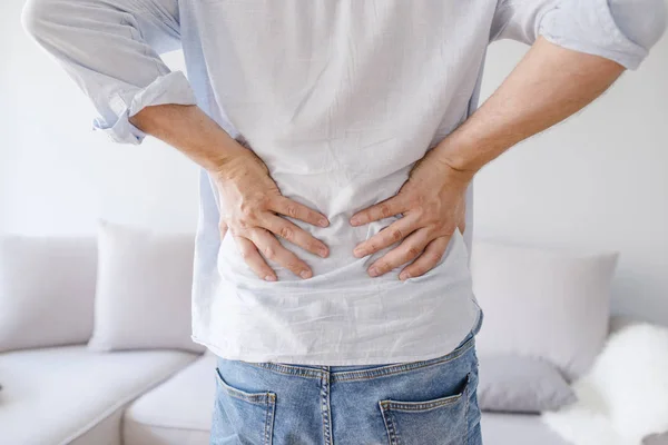 男人在抚摸他的背部 因为它疼 背痛概念弯曲在痛苦与手拿着下背部 关闭的人揉他痛苦的背部 脊椎治疗的概念 — 图库照片