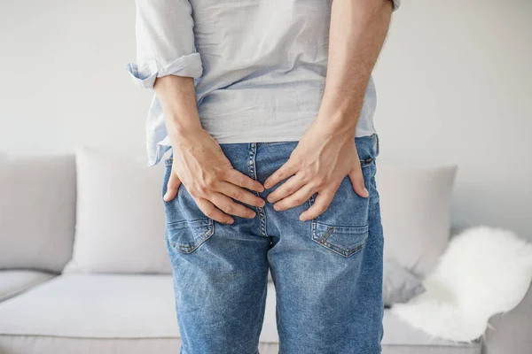 Gri renkle izole acı içinde onun alt tutan adam. Hemoroid kıçını acı içinde tutan adam. Ağrı hemoroid tarafından neden.