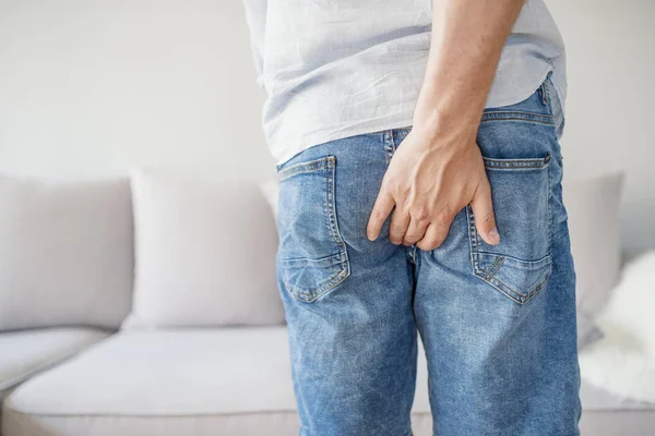 Genç adam, popo, hemoroid, Anal bozukluklarında ağrı vardır. Adam Mavi Jeans kıçını eliyle tutarak acıyla. Anüs içinde kaşıntı. Rektum çatlaklar nedeniyle acı