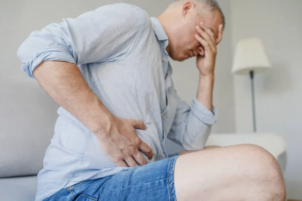 Terrible stomachache. Frustrated handsome young man hugging his belly and keeping eyes closed. Disturbed male having pain in stomach — Stock Image Terrible Stomachache Frustrated Handsome Young Man Hugging His Belly Keeping Stock Picture