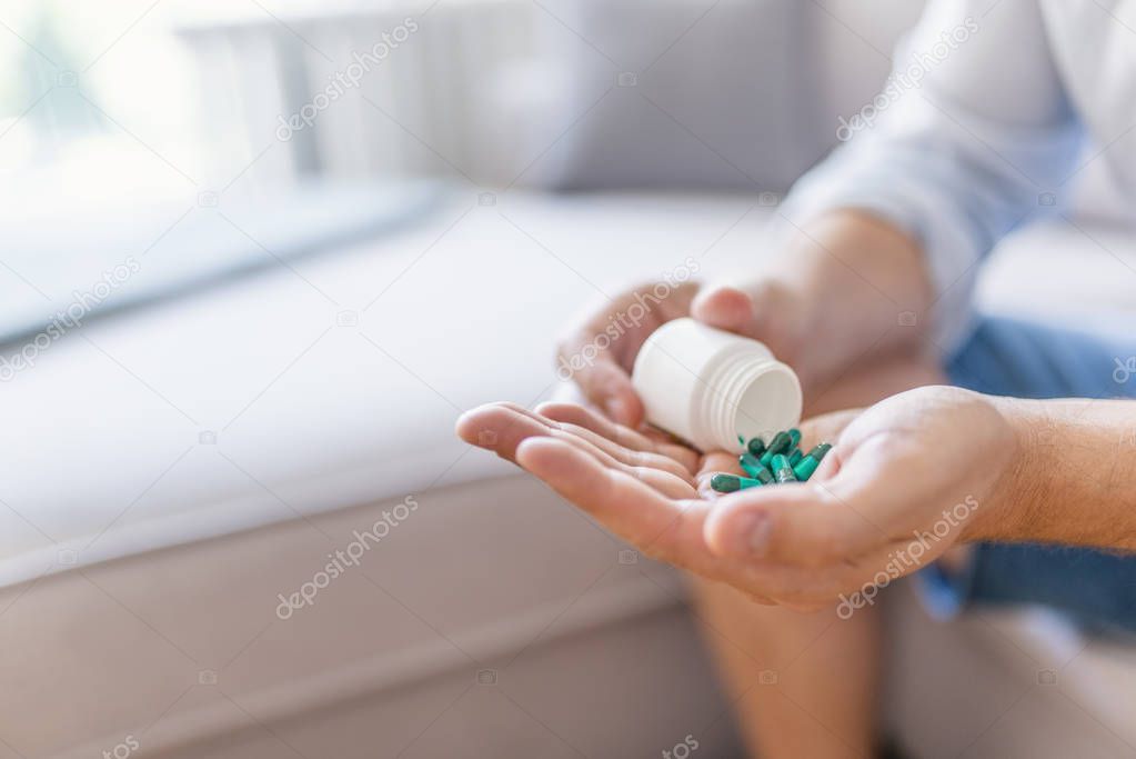 Man holding pills on hand. Pills in hands. Medicine and health care concept. Hand spilling pills for the pain of a bottle in the living room. Healthy lifestyle, medicine, nutritional supplements and people concept 
