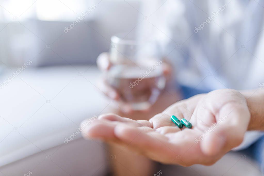 Medicine, health care and people concept - close up of man taking in pill. Close-up view of man holding pill in one hand and glass of water in the another hand. Focus on the pill