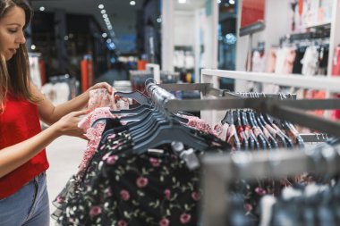 Genç kadın bir galeride bir raf üzerinde giysiler seçmek. Güzel kadın trendy kıyafetler alışveriş. Alışverişkoliğin kadın elbisesi satış alışveriş. Alışveriş, moda, stil ve insanlar kavramı 