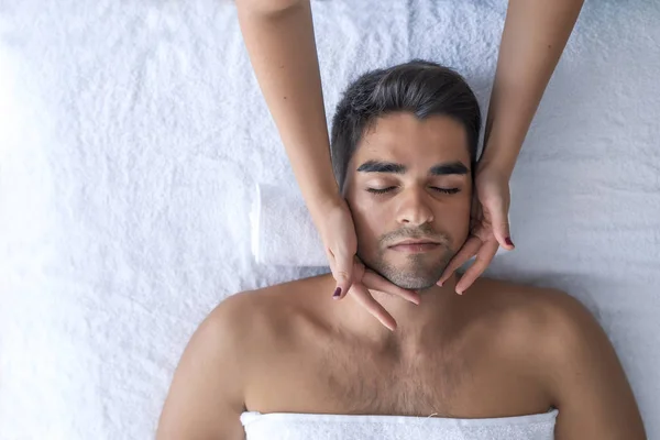 Masseur doing head massage at man in spa salon
