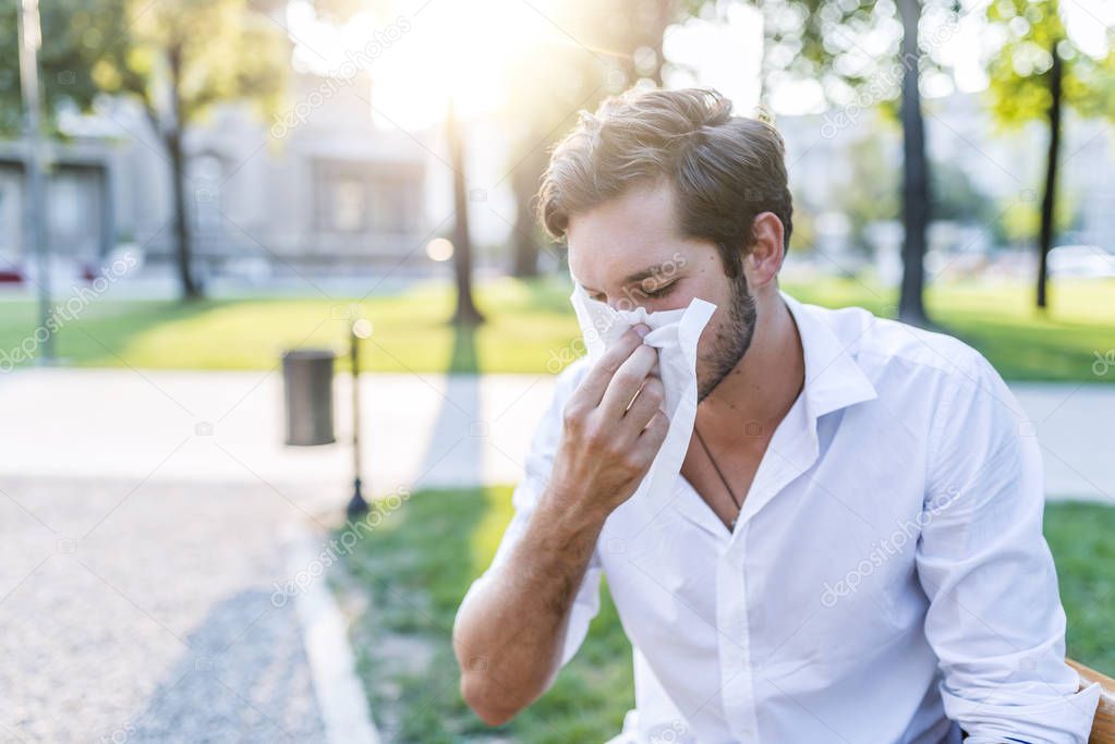 Portrait of young man with allergy blowing nose with tissue