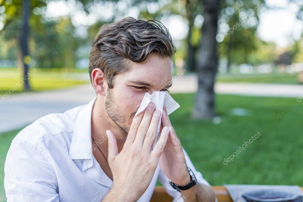 Portrait of young man with allergy blowing nose with tissue