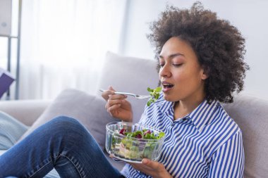 Oturma odasında kanepede salata yemek güzel Afrikalı-Amerikalı kadın