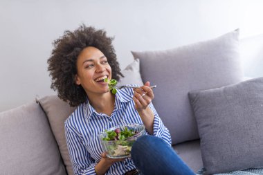 Oturma odasında kanepede salata yemek güzel Afrikalı-Amerikalı kadın