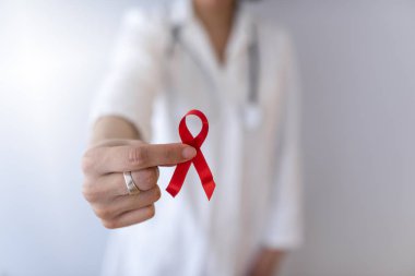 Kadın doktor elinde kırmızı kanser farkındalığı kurdelesi tutuyor.