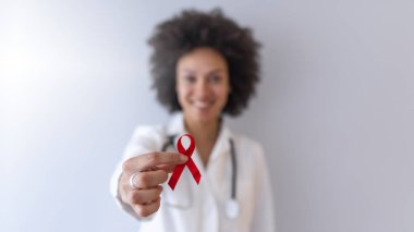 Kadın doktor elinde kırmızı kanser farkındalığı kurdelesi tutuyor.