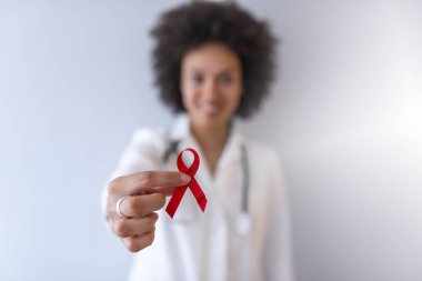 Kadın doktor elinde kırmızı kanser farkındalığı kurdelesi tutuyor.