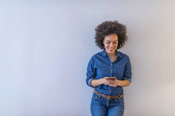 愉快的非洲裔美国妇女站在灰色的背景 拿着手机 — 图库照片
