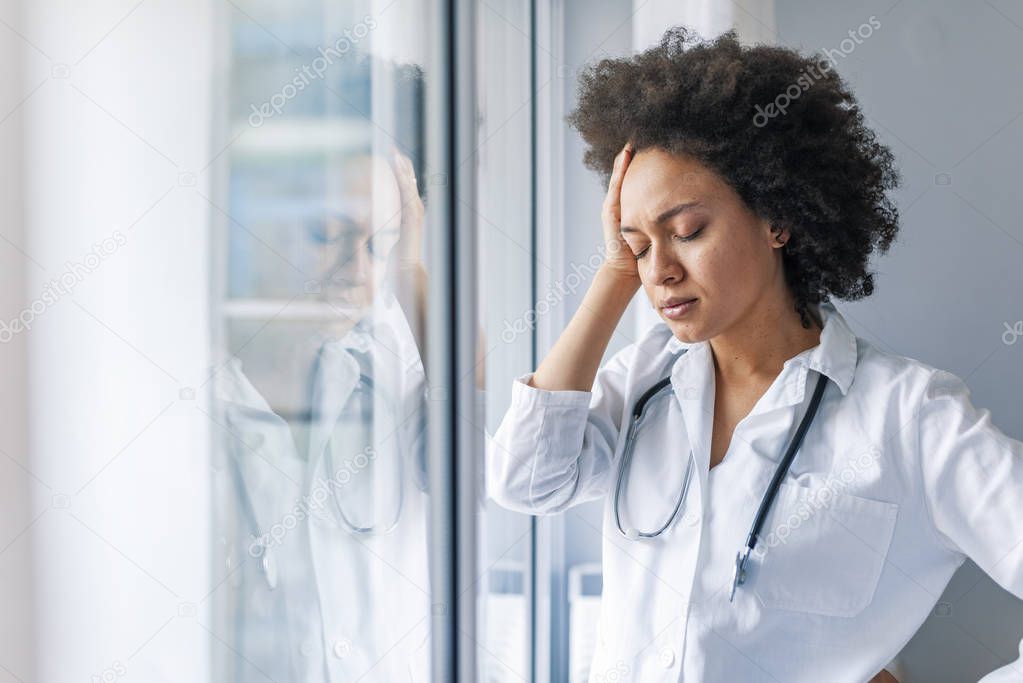 Tired stressed female doctor standing near window