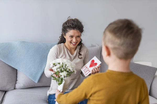 Glad Son Gratulera Mamma Och Ger Vykort Och Blommor Soffa — Stockfoto