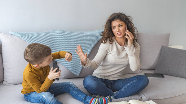 Многозадачная занятая мать разговаривает по телефону, пока маленький сын играет

