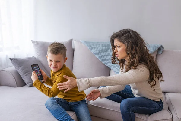 Mother scolding child boy playing with phone on couch