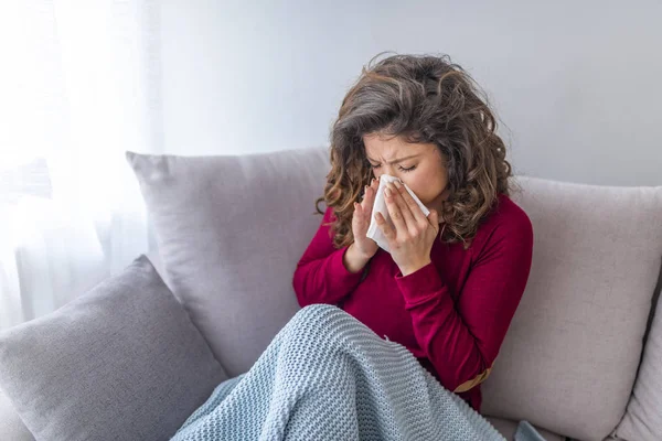 Young girl sick in bed with temperature sneezing into tissue and holding fever drinking cup of warm tea