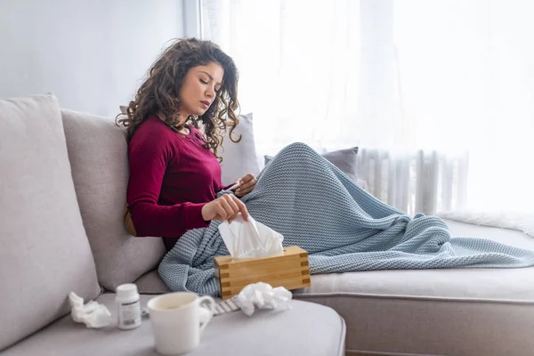 悲惨な女性が毛布に包まれたベッドの上に座ってのインフルエンザと病気を感じて 熱を持つ ハンカチで鼻水を吹いて — ストック写真