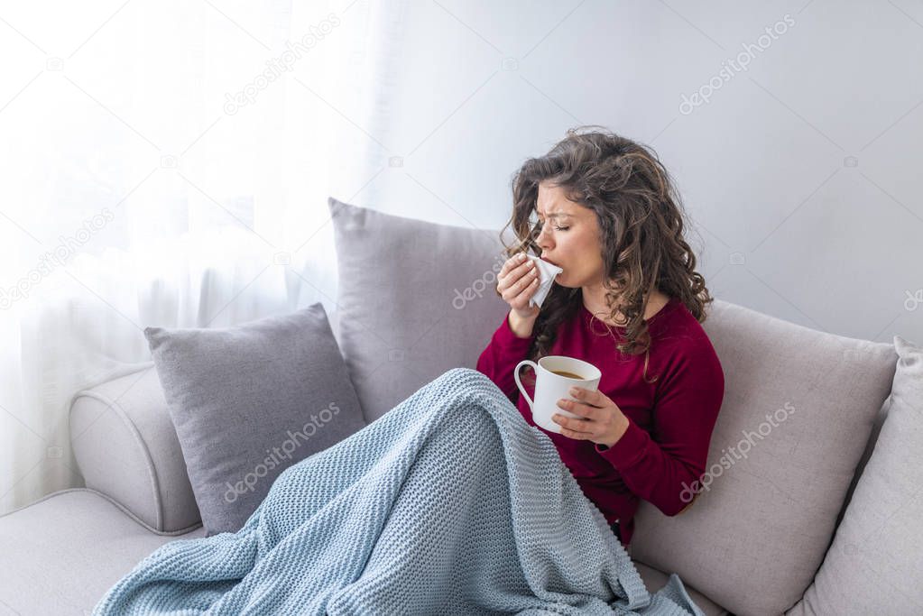 Young girl sick in bed with temperature sneezing into tissue and holding fever drinking cup of warm tea