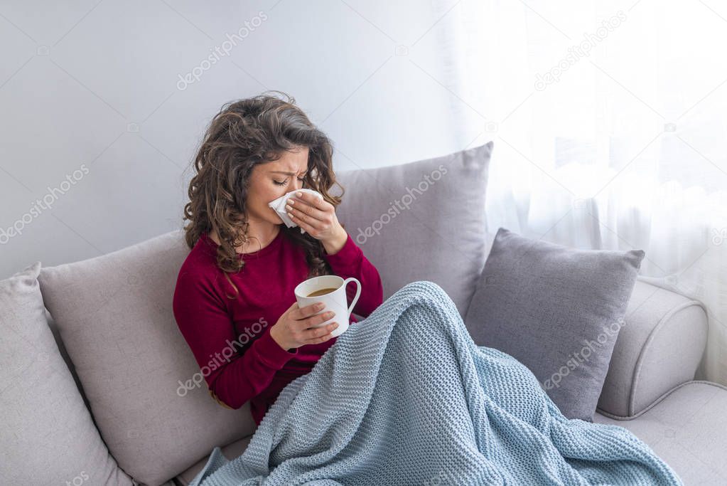 Young girl sick in bed with temperature sneezing into tissue and holding fever drinking cup of warm tea