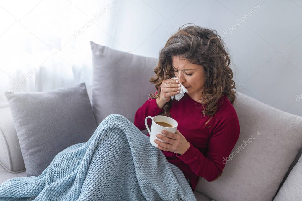 Young girl sick in bed with temperature sneezing into tissue and holding fever drinking cup of warm tea