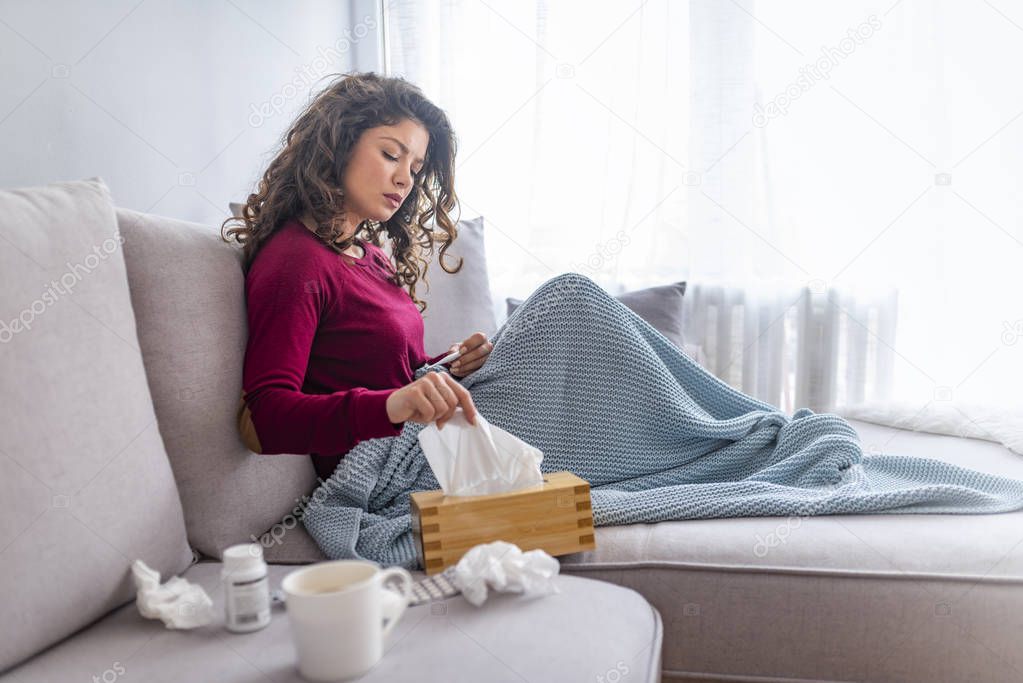 Miserable woman sitting on the bed wrapped in blanket, feeling sick with flu, having fever and blowing runny nose with handkerchief