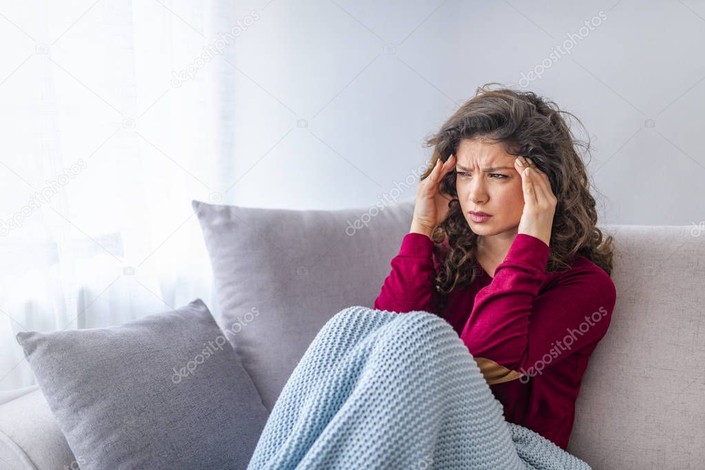 Young woman sitting on a couch and having strong headache
