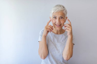 Yakışıklı, güzel, mükemmel yumuşak yüzünü dokunaklı yaşlı kadın cilt parmakları ile gün, gece yüz kremi, kozmetik prosedürler kullanarak gri arka plan üzerinde kameraya gülümseyen