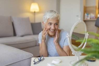 Yaşlı kadın aynanın önünde yüze dokunuyor, yakın çekim. Aynaya bakan orta yaşlı çekici bir kadının portresi. Çekici yaşlı kadın aynada kendine bakıyor