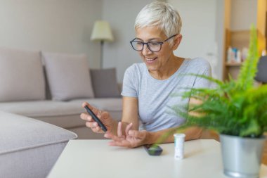 Evde kan şekeri seviyesini kontrol glucometer ile mutlu olgun kadın. Yüksek kan şekeri testi olan kadın. Kan şekerini ölçmek için kadın tutma cihazı