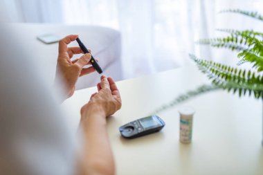 Kandaki glikoz seviyesini test alan kadının yakın çekim fotoğrafı. Kan şekeri ölçümü yapan lancet ve glucometer kullanan olgun kadın.