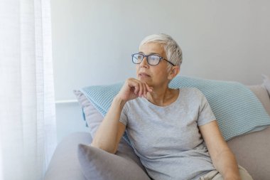 Olgun gri saçlı kadın evde poz kanepede oturan.