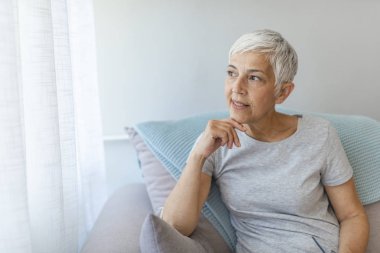 Olgun gri saçlı kadın evde poz kanepede oturan.